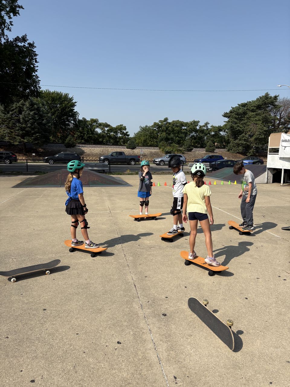 Young skaters lined up on skateboards with cones set up for a balance drill during a Skate Lessons Chicago class at Hinkley Skate Park in Park Ridge