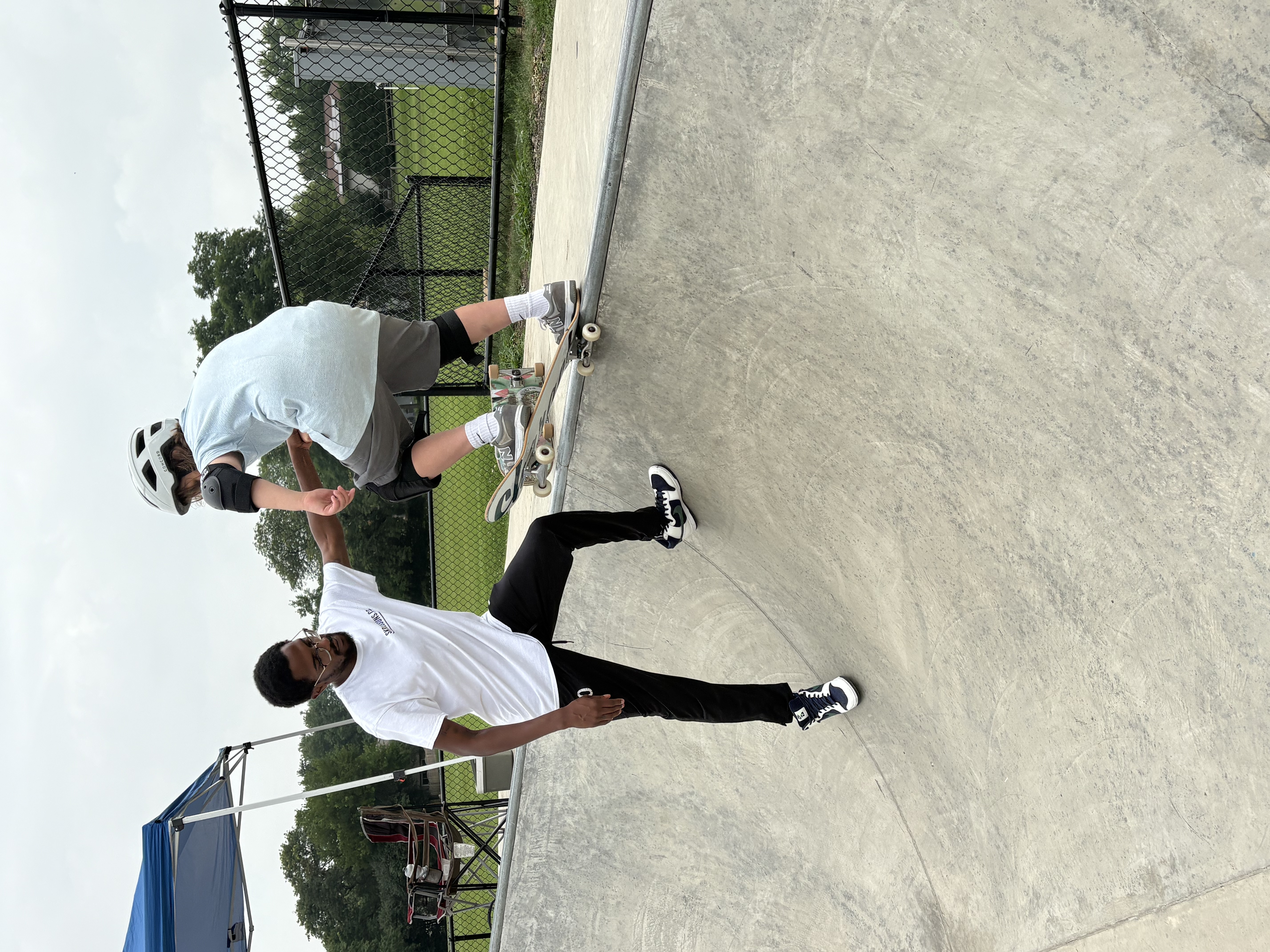 A coach helping a young skater drop into a skatepark bowl on a skateboard